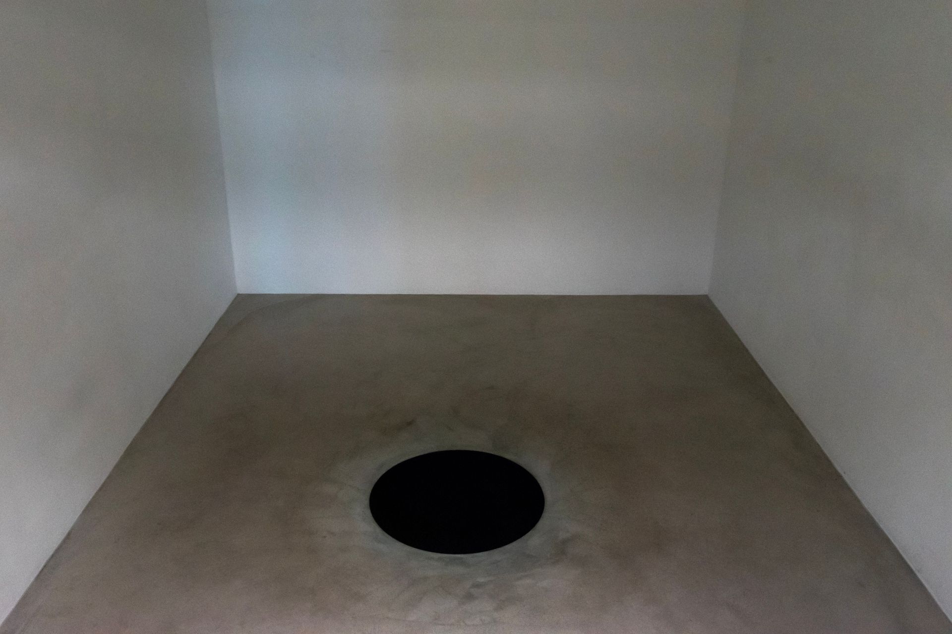 Empty white room with a circular hole in the floor near the center.