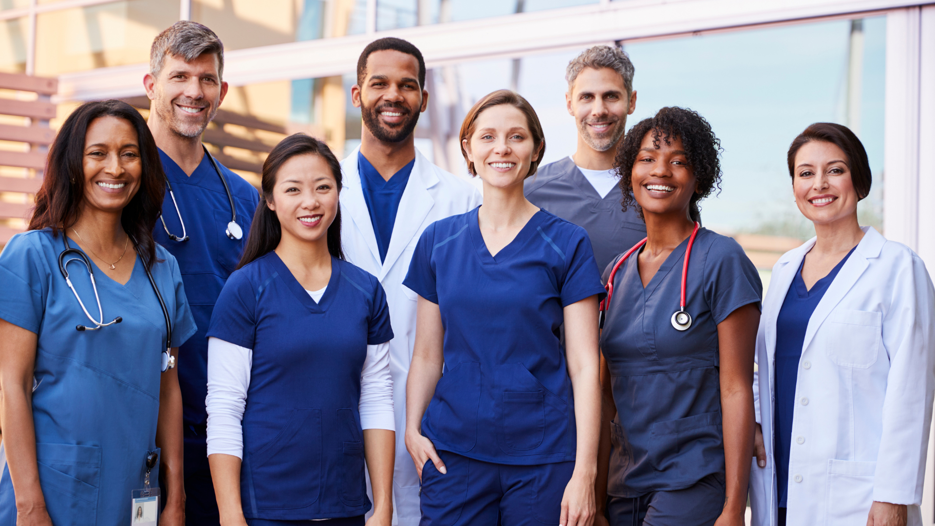 A group of doctors and nurses are posing for a picture in front of a hospital building.