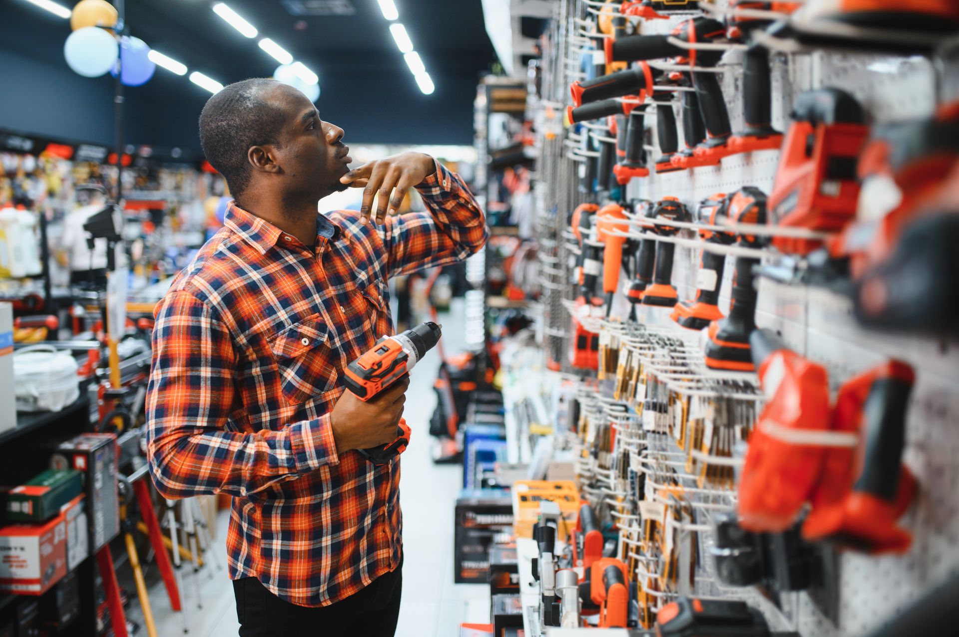 Man in plaid shirt examining power tools on display in hardware store.