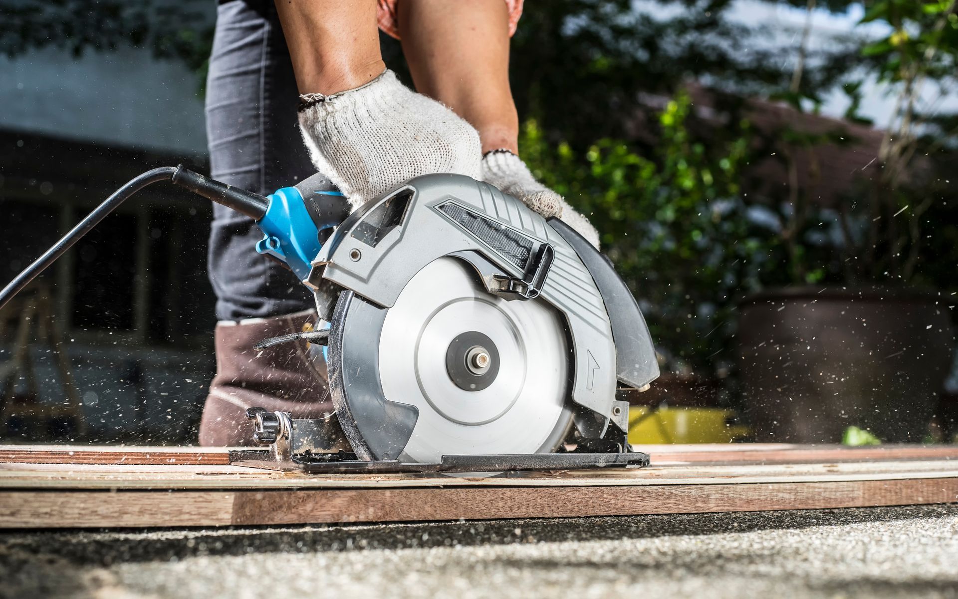 A cropped view of a carpenter using a circular saw for cutting wooden boards.