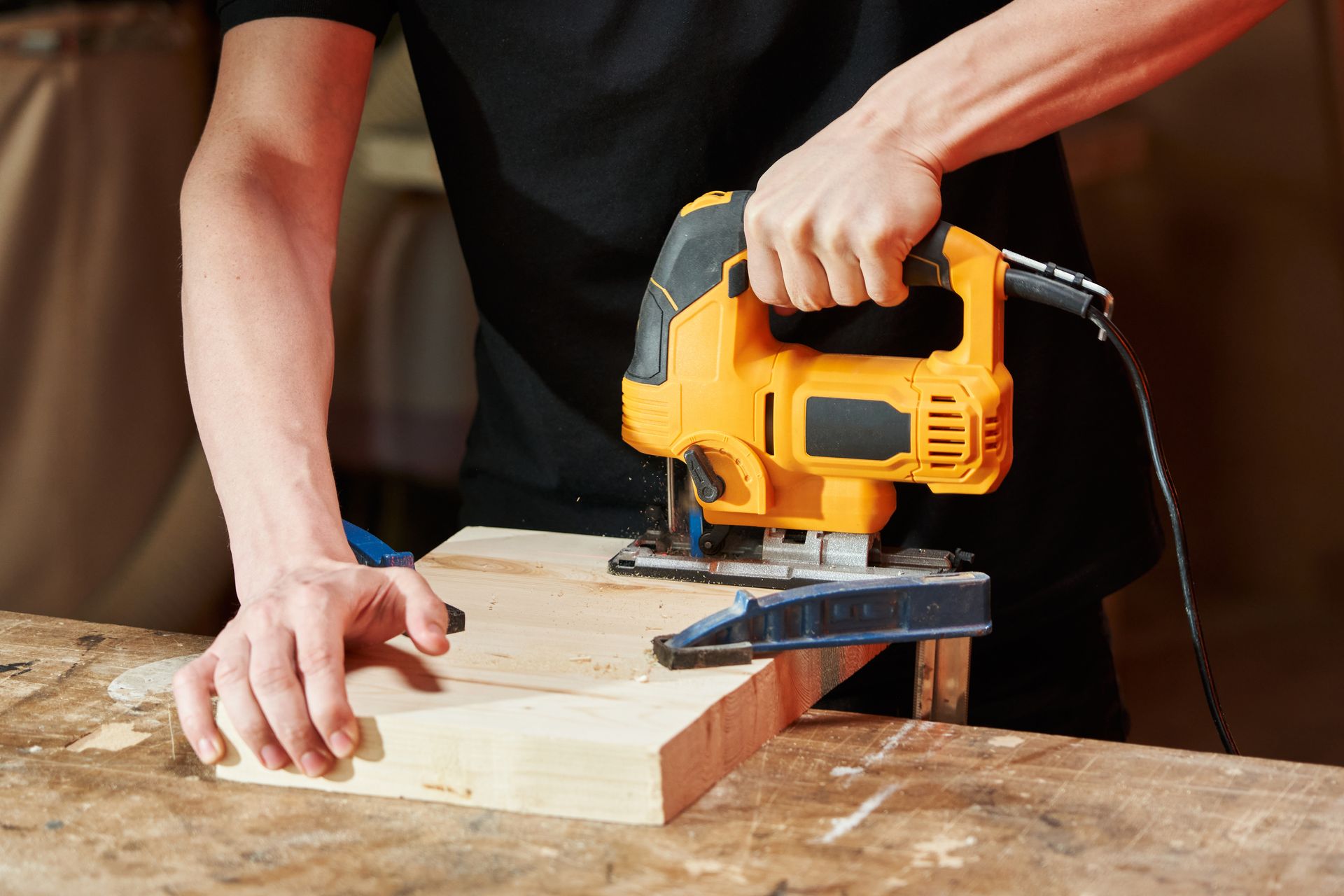 Person using an orange jigsaw to cut a wooden plank on a workbench.