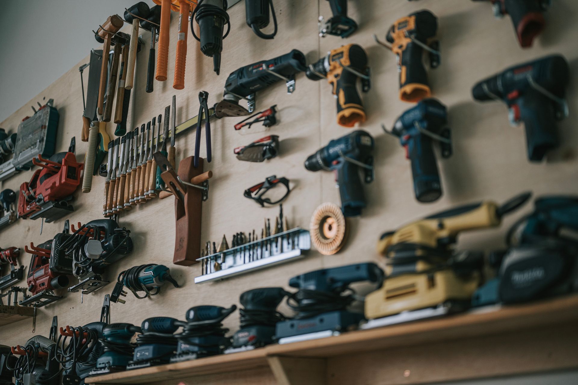 Wall-mounted tool rack with power tools and hand tools in workshop.