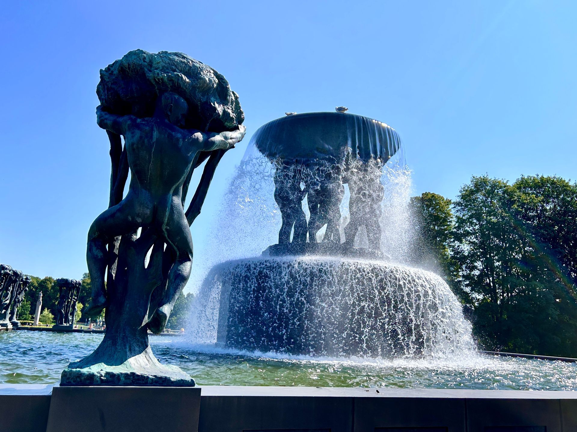 A statue at the Vigeland Park next to a fountain showing multiple men carrying a large bucket of water. 