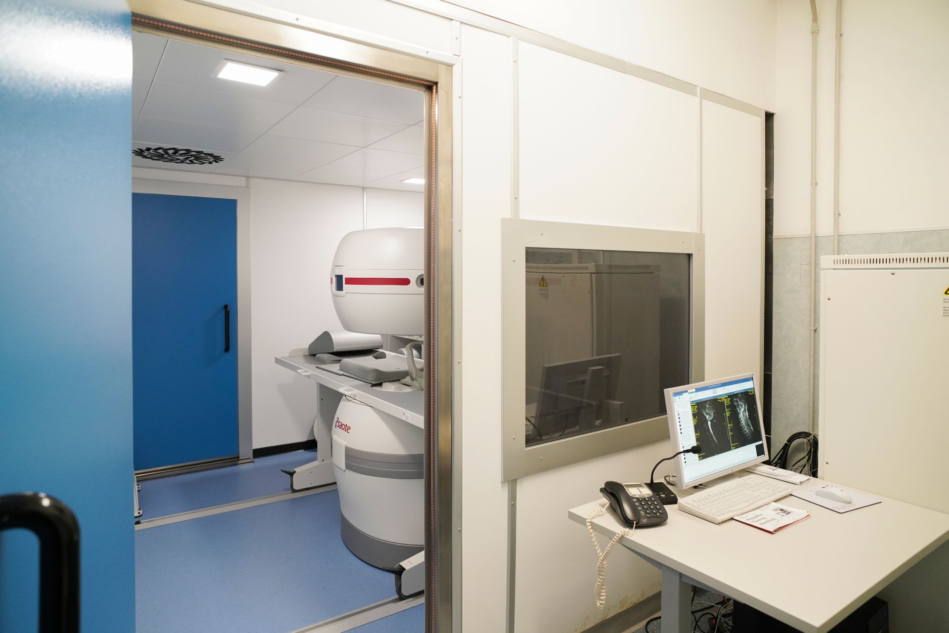 Una stanza con una macchina per la risonanza magnetica e un computer su una scrivania.