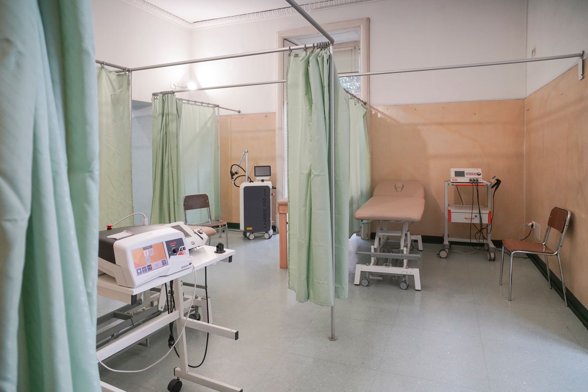 Una stanza d'ospedale con tende verdi, un tavolo e delle sedie.