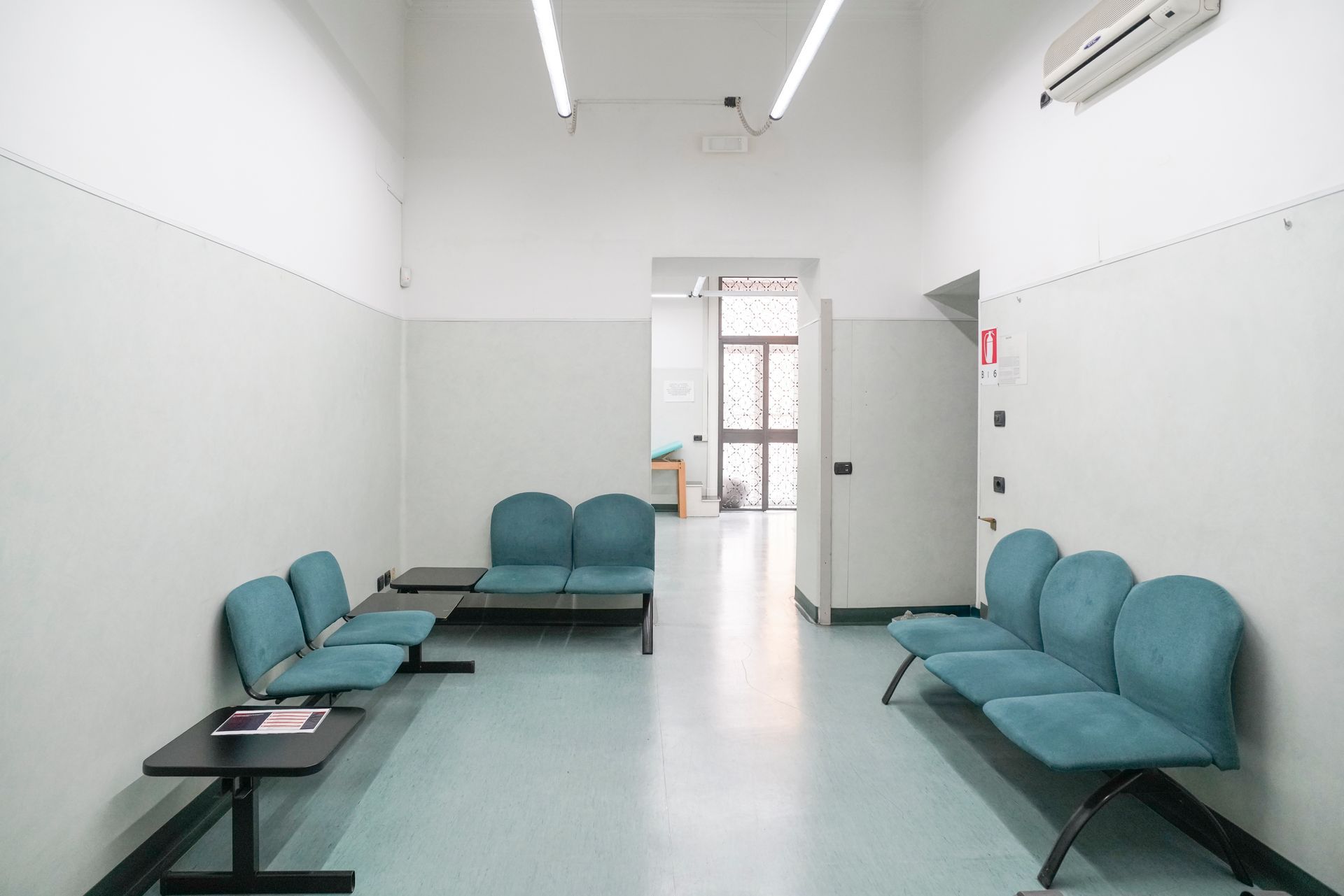 Una sala d'attesa vuota con sedie blu e un tavolo.