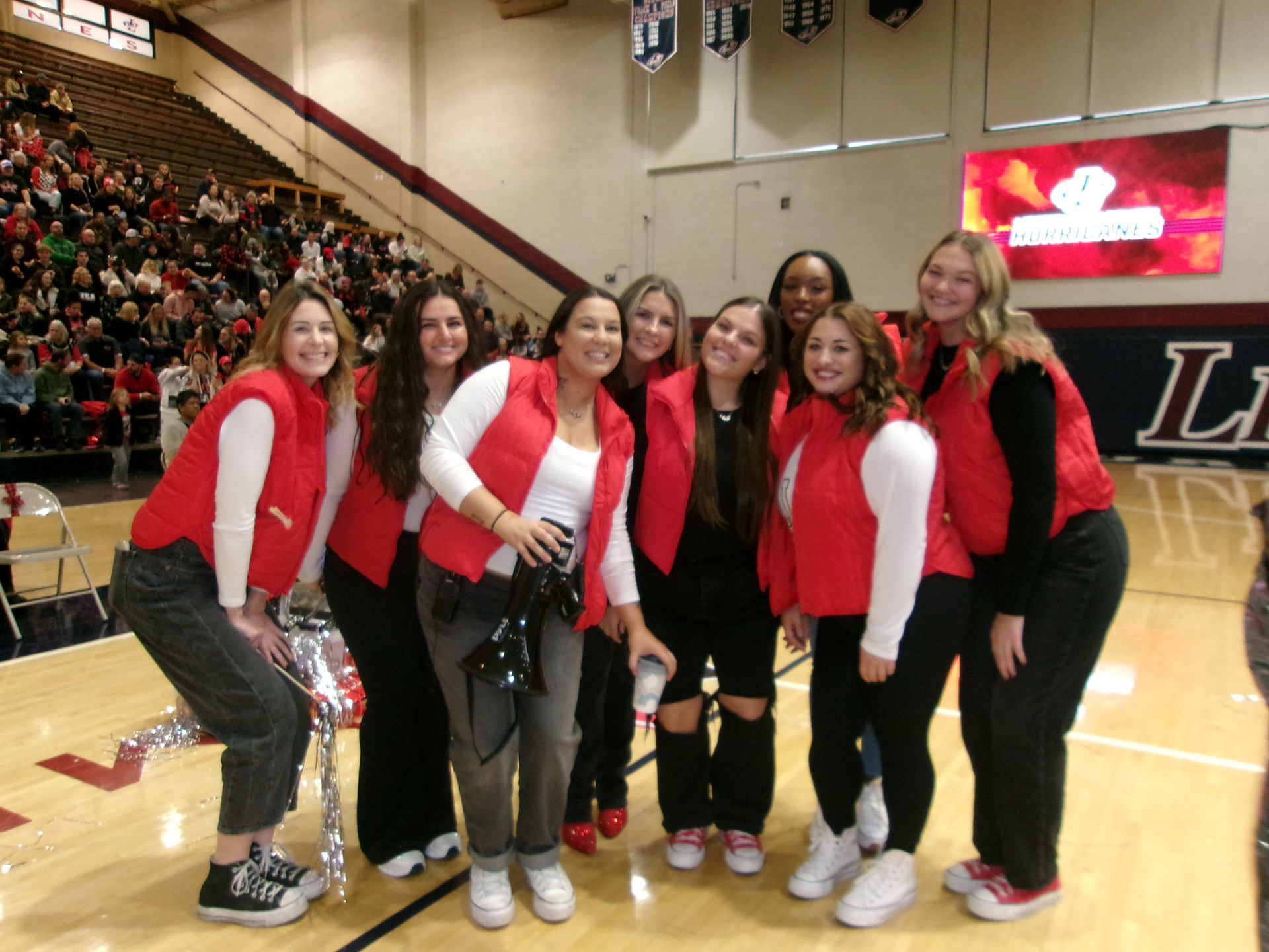 A group of people wearing matching red vests and white tops stand together on a basketball court.