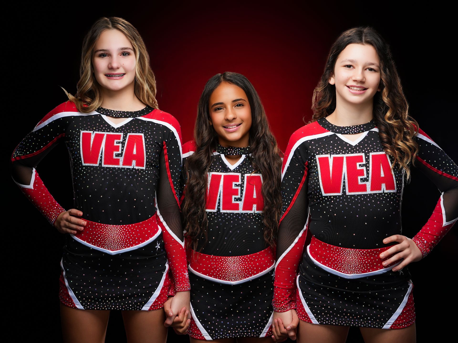 Three smiling cheerleaders in matching black, red, and white uniforms with 