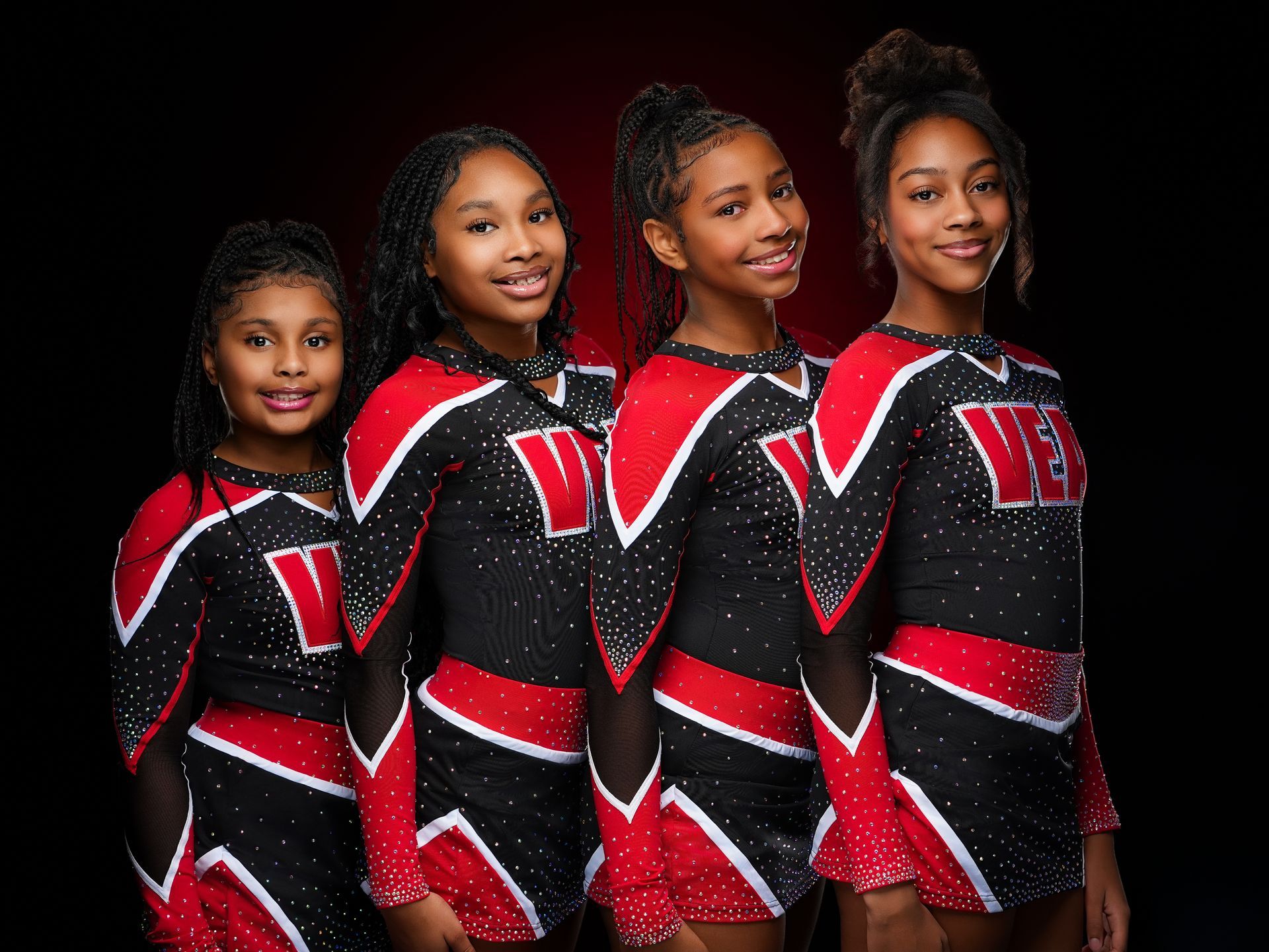 Four cheerleaders wearing matching red, black, and white uniforms pose against a dark background.