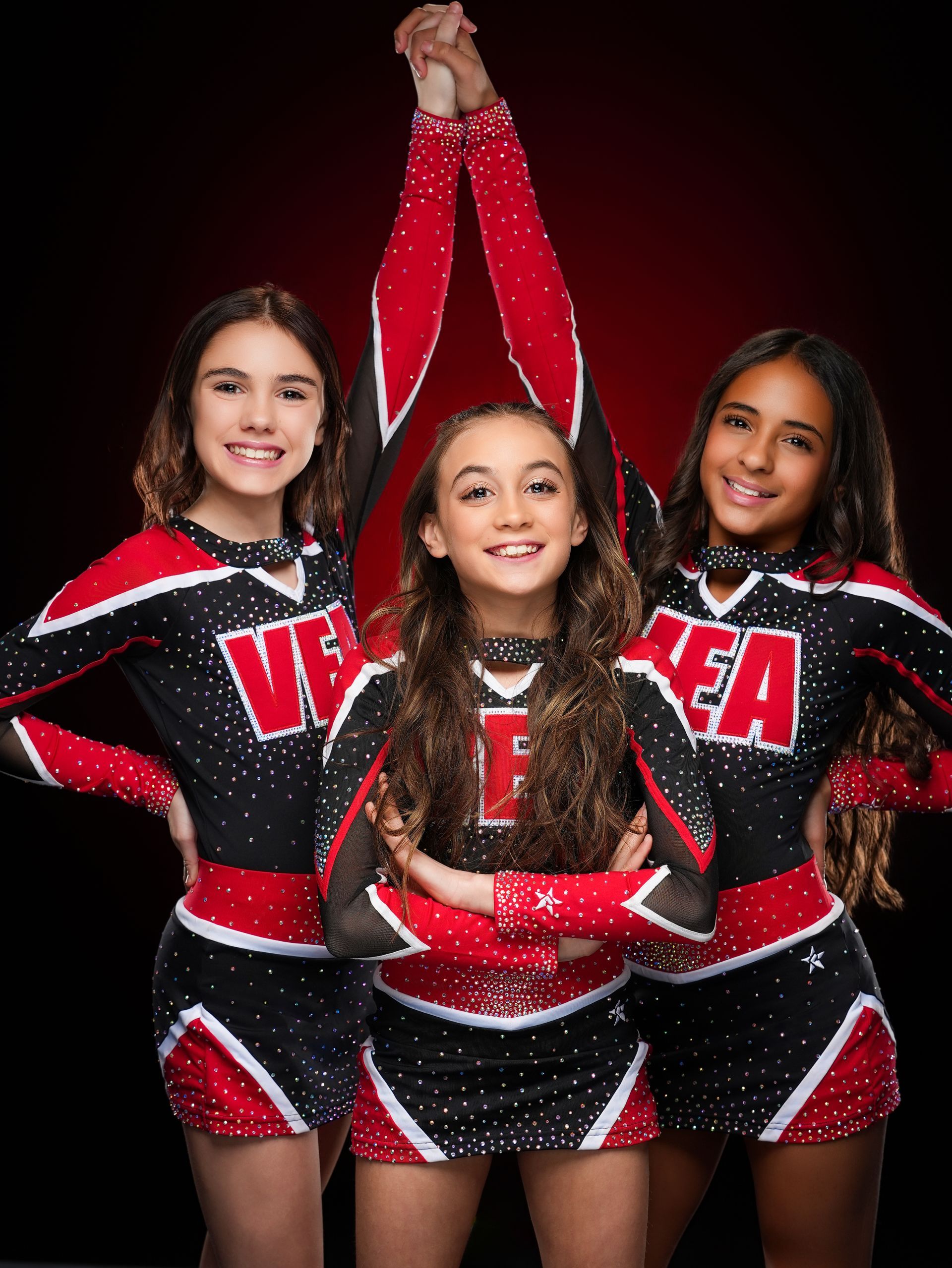 Three cheerleaders in black and red uniforms pose against a dark background, with the center cheerleader posing arms up.