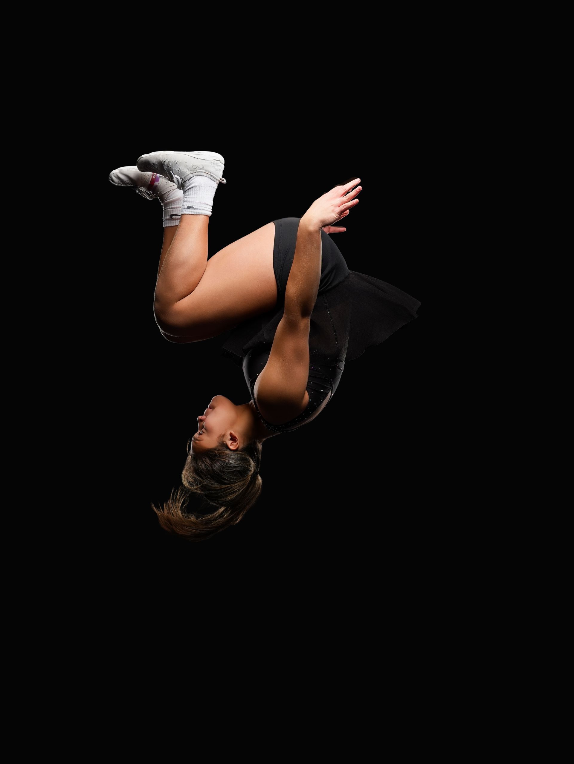 A person in a black athletic outfit performs a backflip against a plain black background.