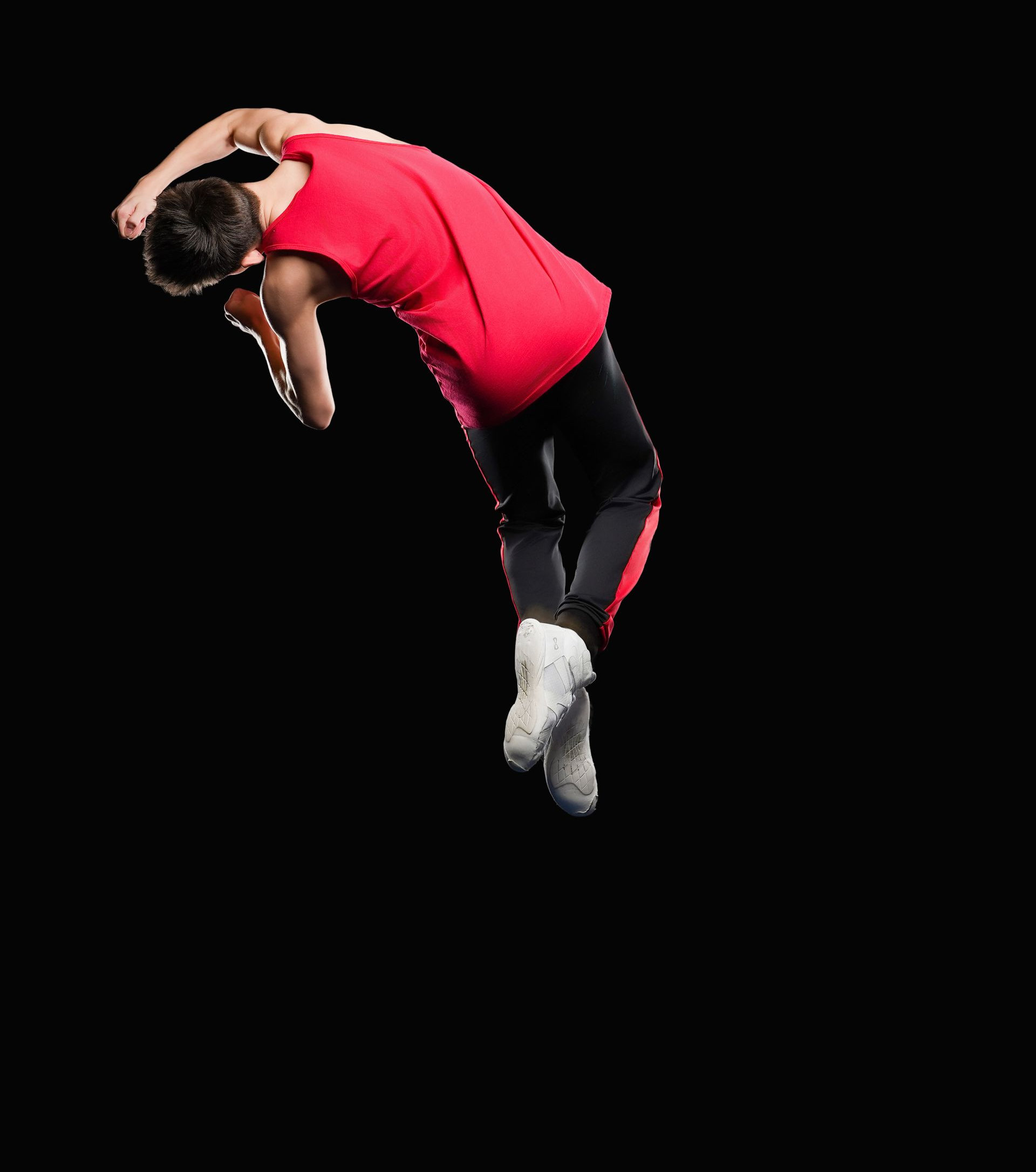 A person wearing a red tank top and dark pants mid-air in a dance pose against a black background.