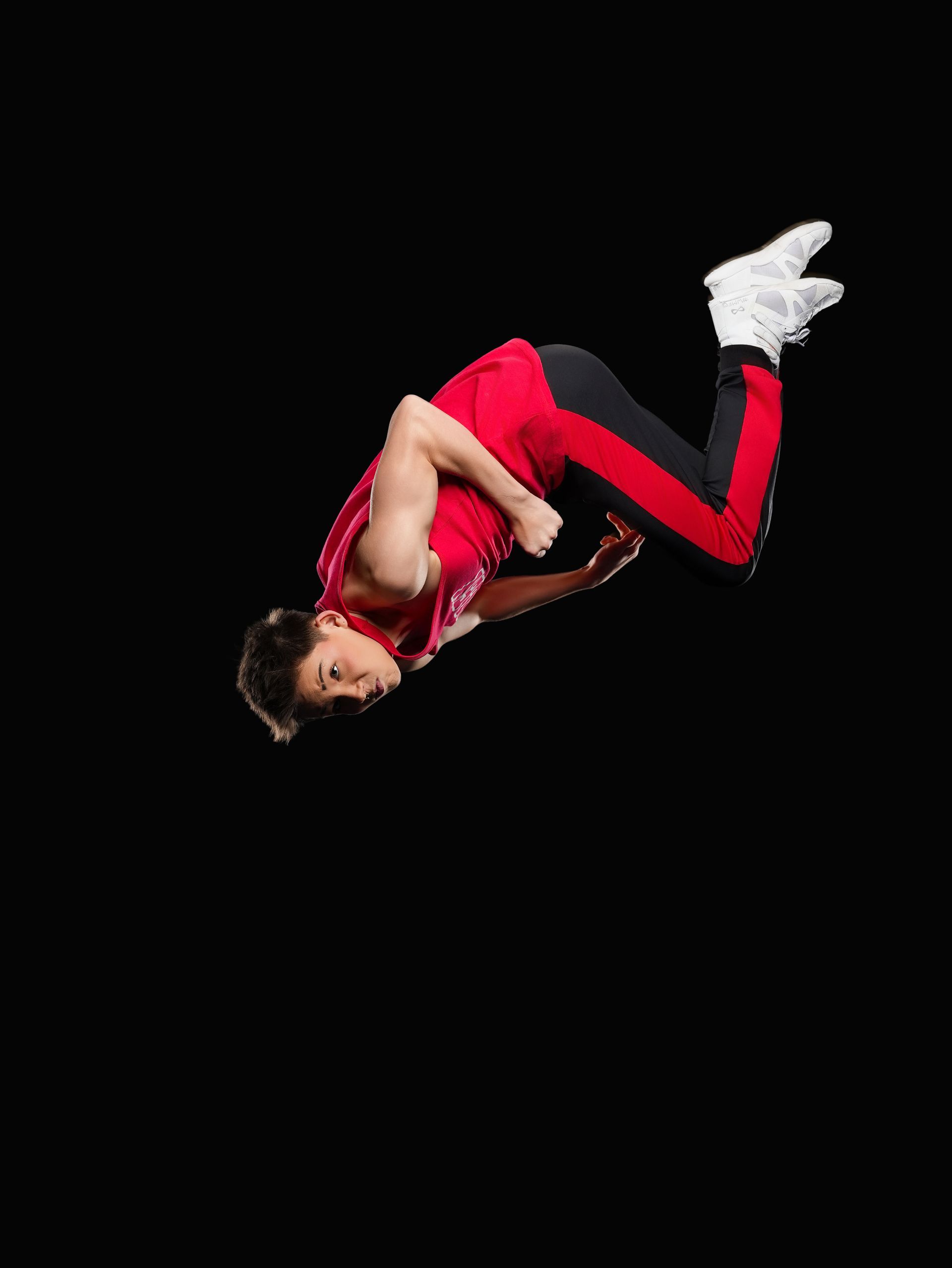 A person wearing a red tank top and black pants with red stripes performs a backflip against a solid black background.