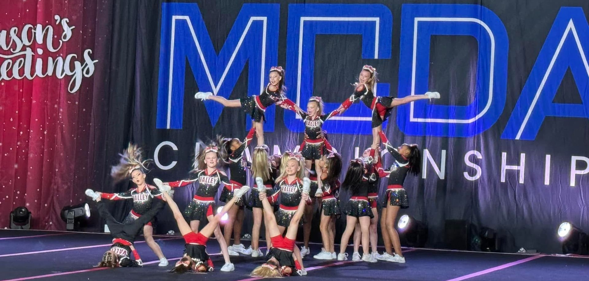 A cheerleading team performs a complex pyramid and tumbling routine on stage at a competition.