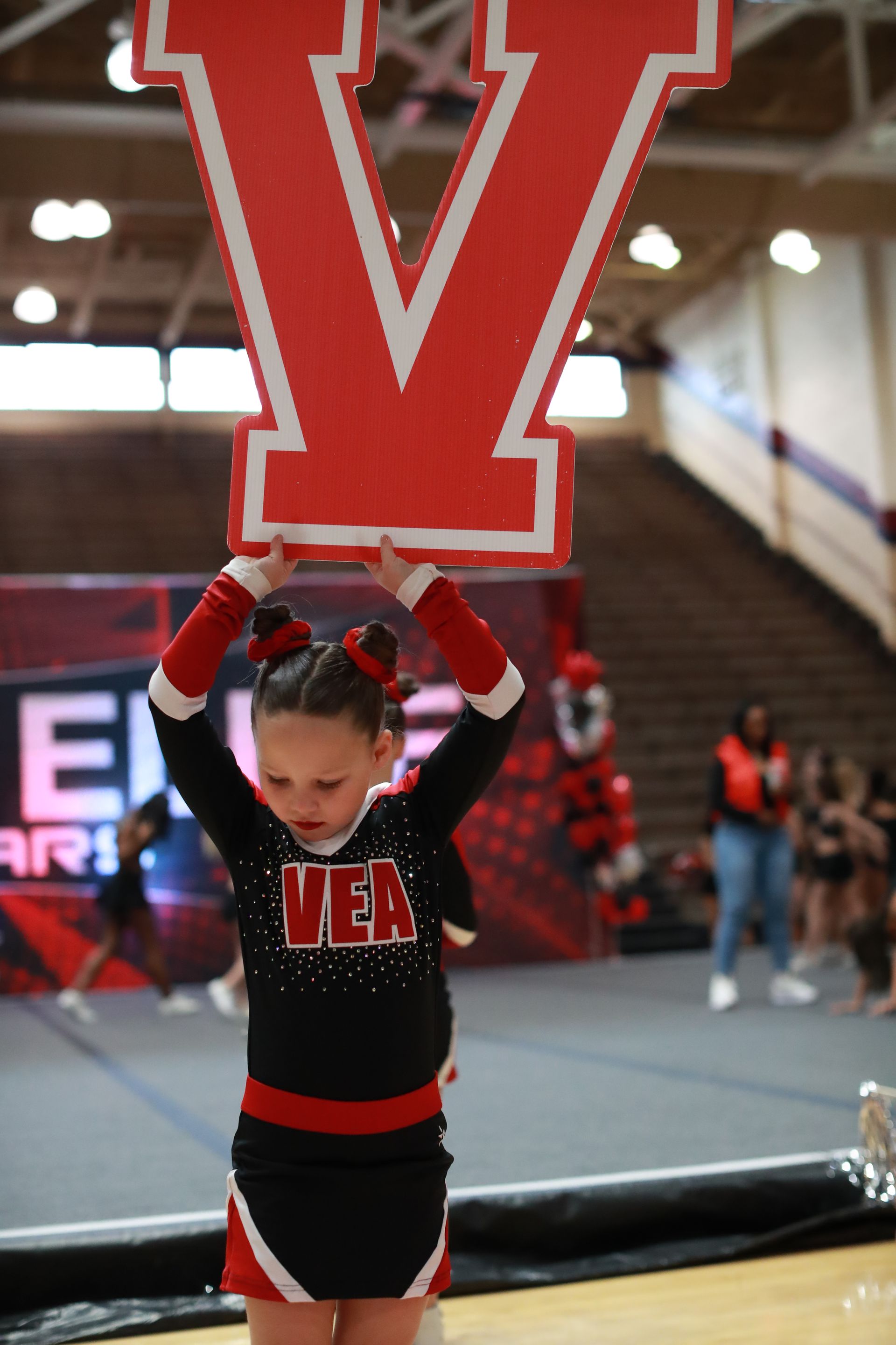 A cheerleader in a black and red uniform holds a large red letter