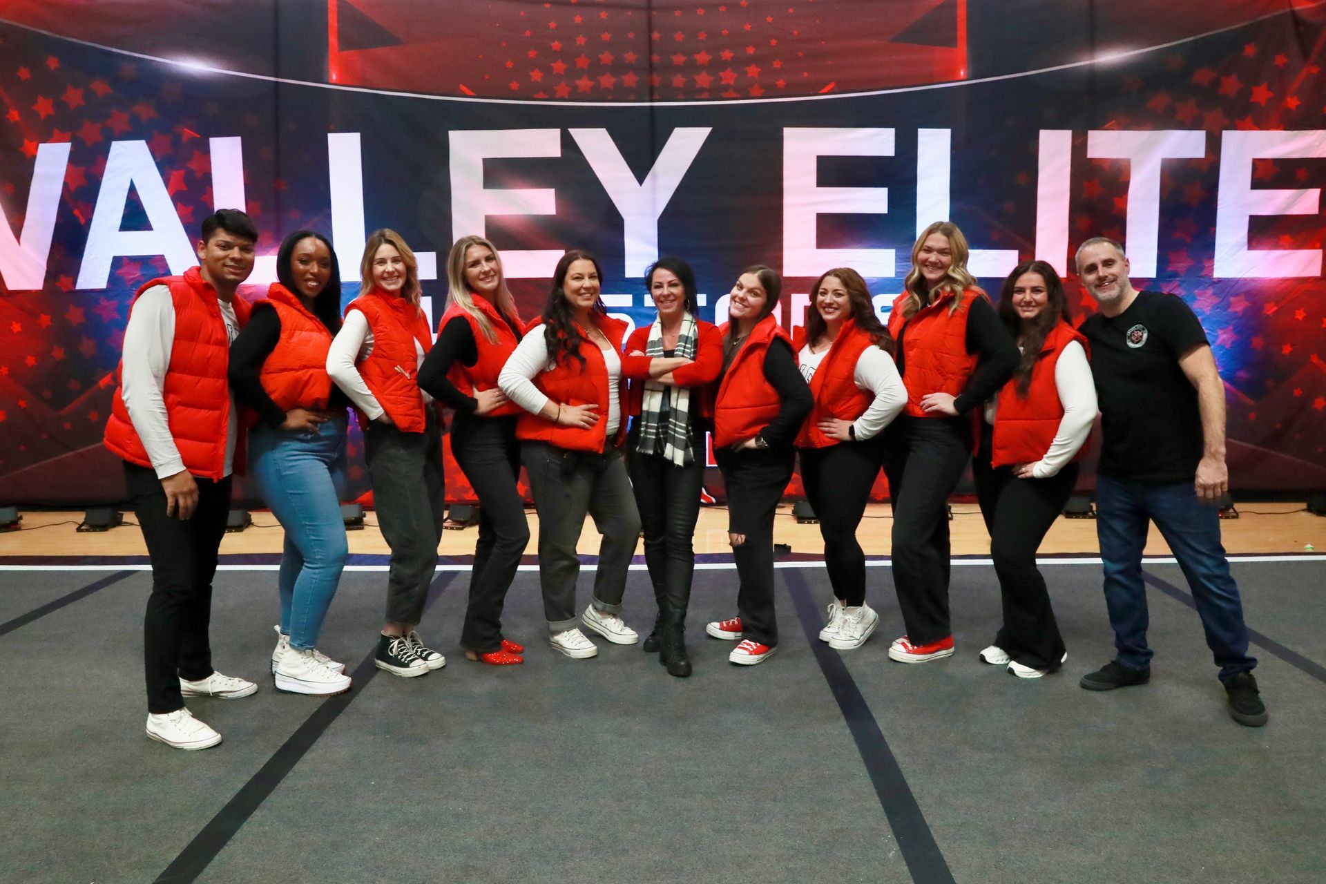 A group of people wearing red vests pose together in front of a digital display that reads 