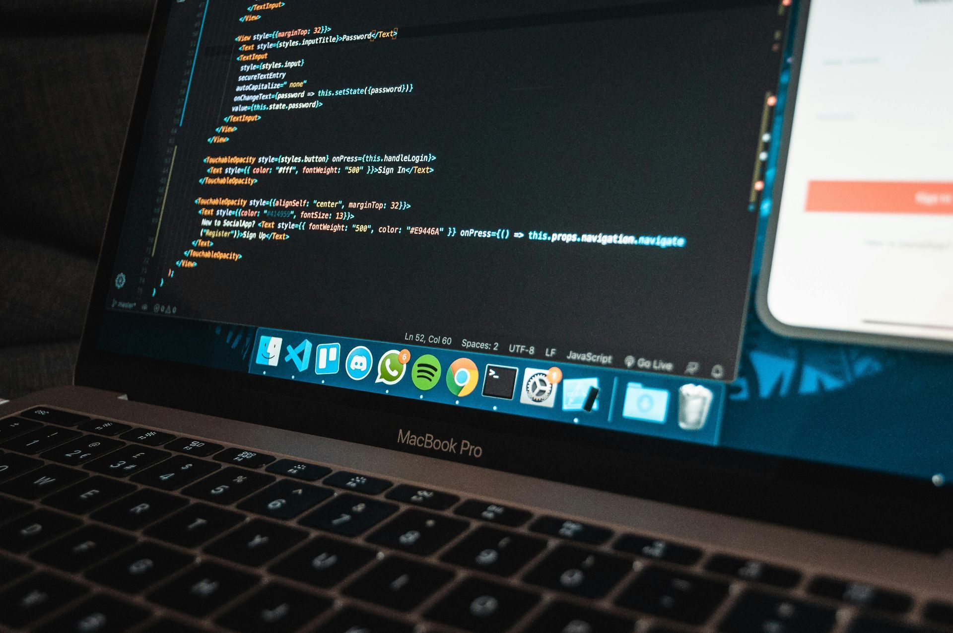 Laptop displaying lines of code with a phone partially visible on the screen, indoors.