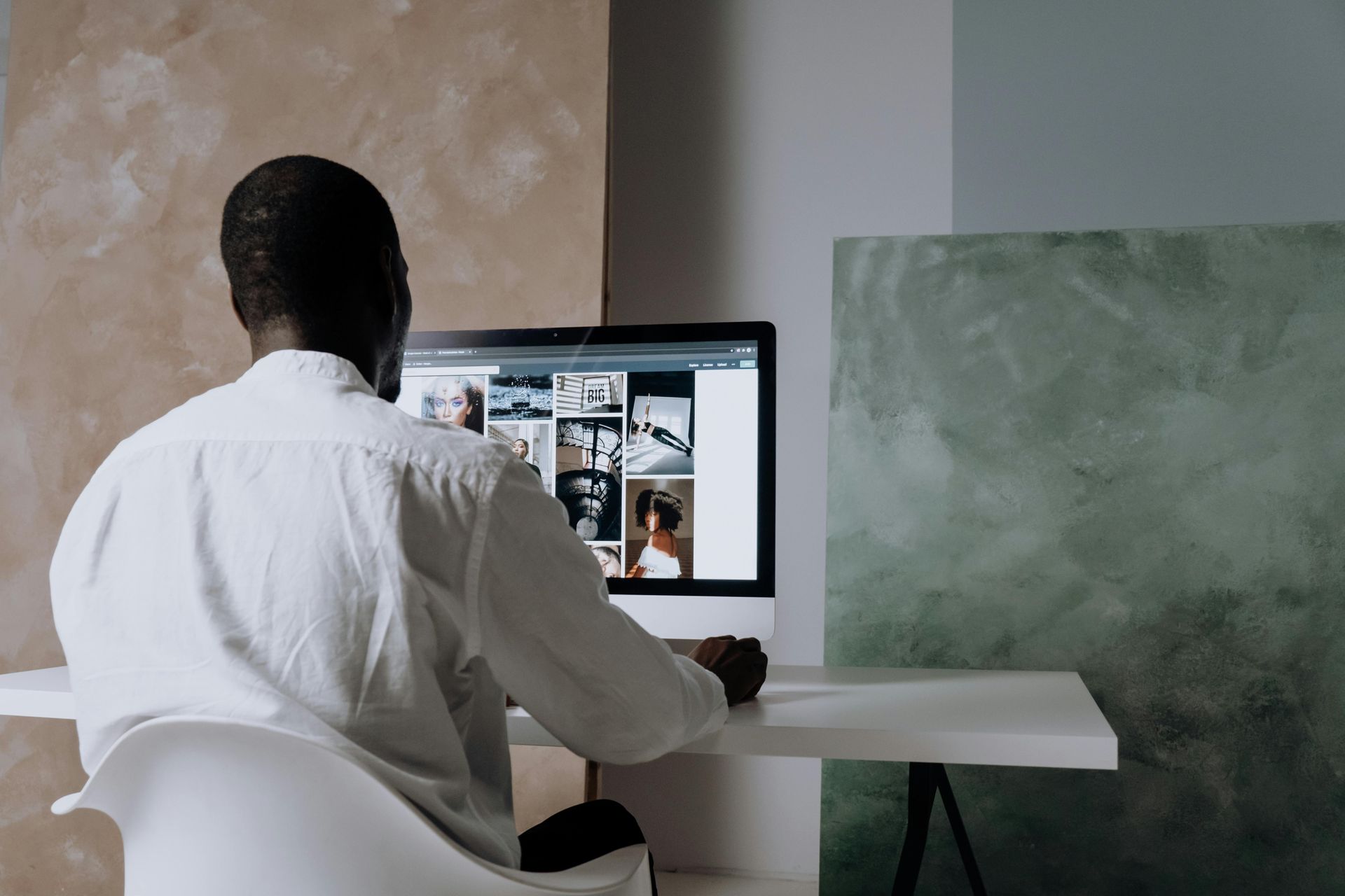 Man in white shirt works at a computer, looking at photos. He's in a bright room with colored wall panels.