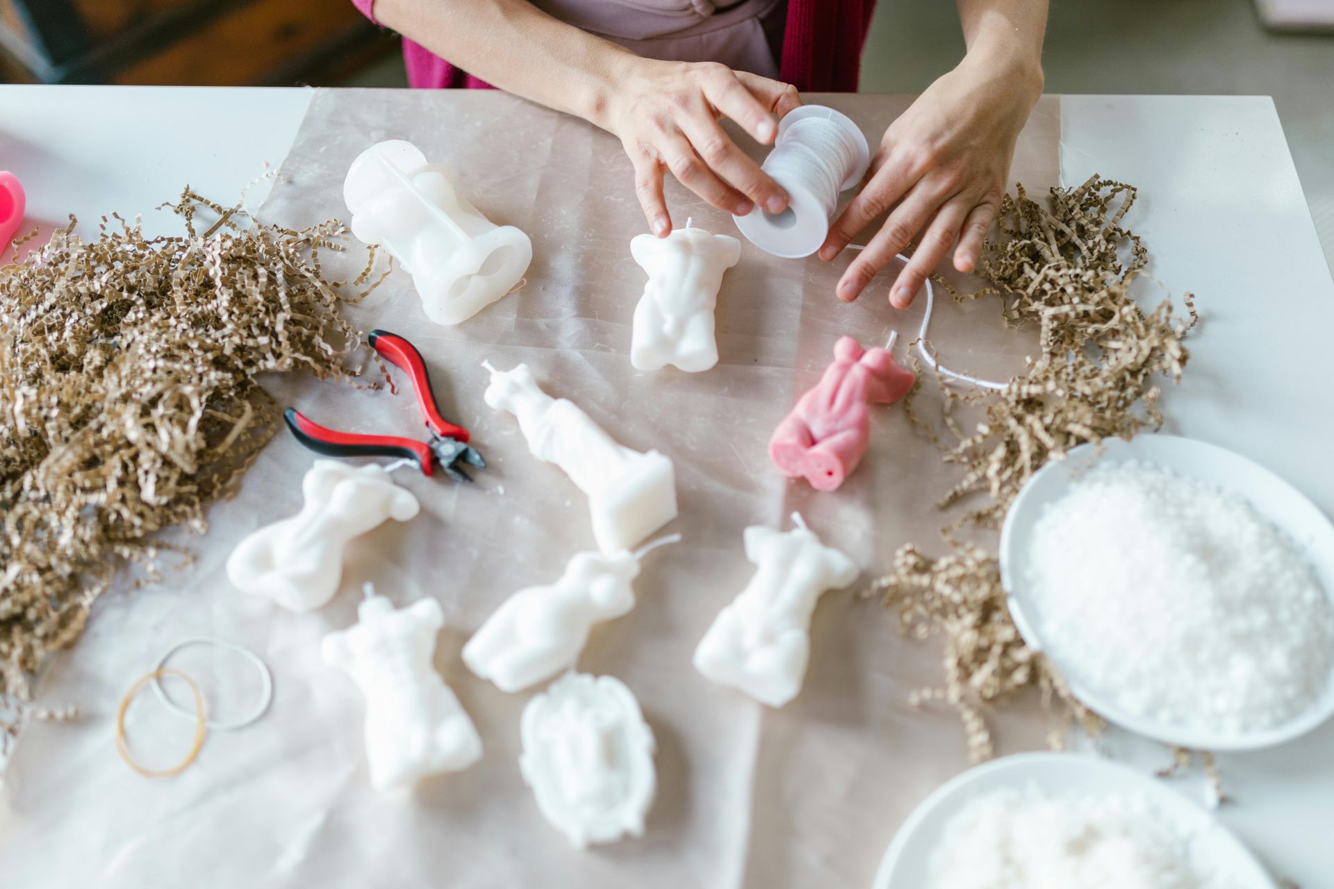 Woman crafting candles in various body shapes. White, pink wax, tools, and ingredients on a table.