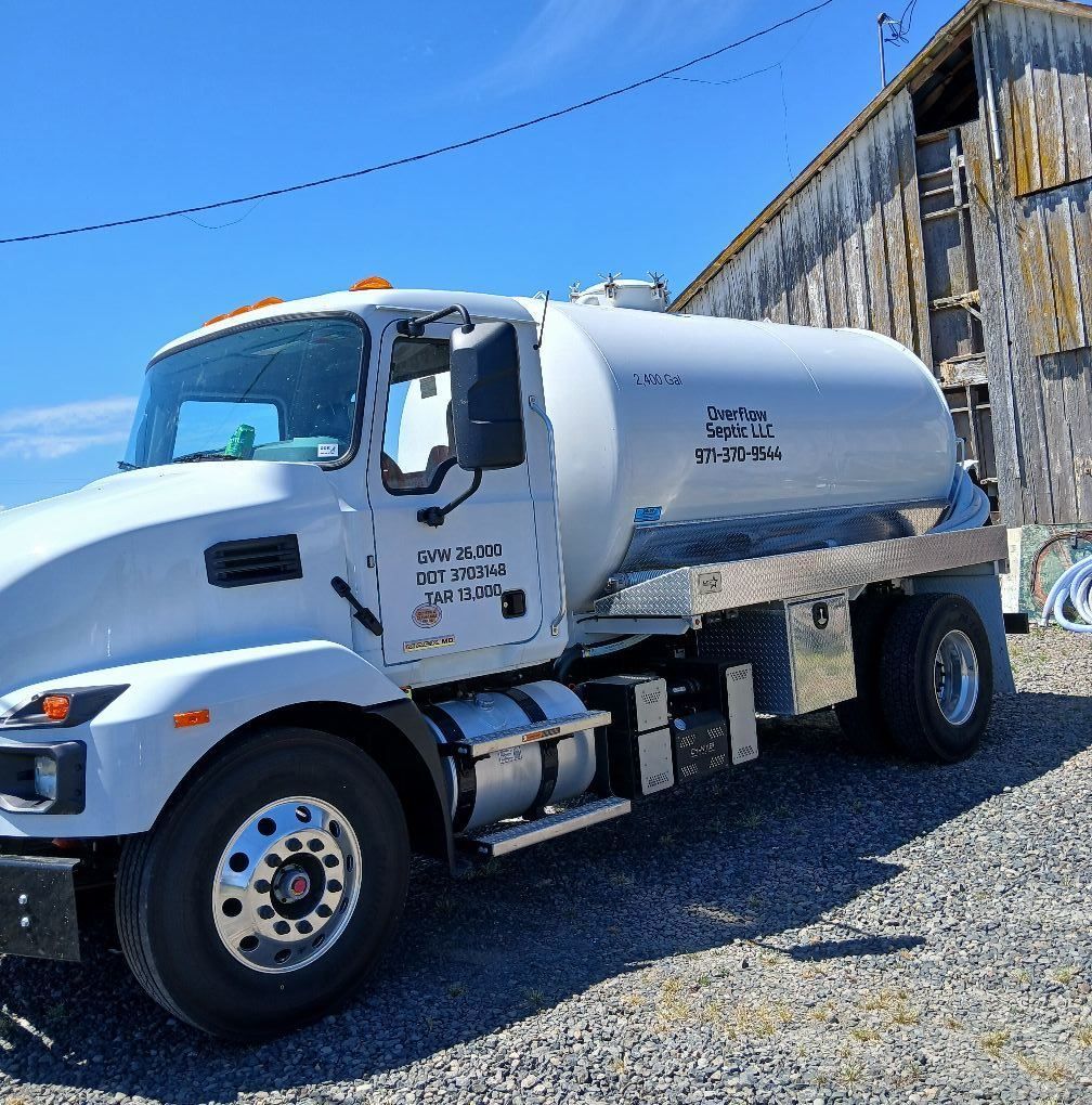 White tanker truck parked by a weathered barn under a blue sky.