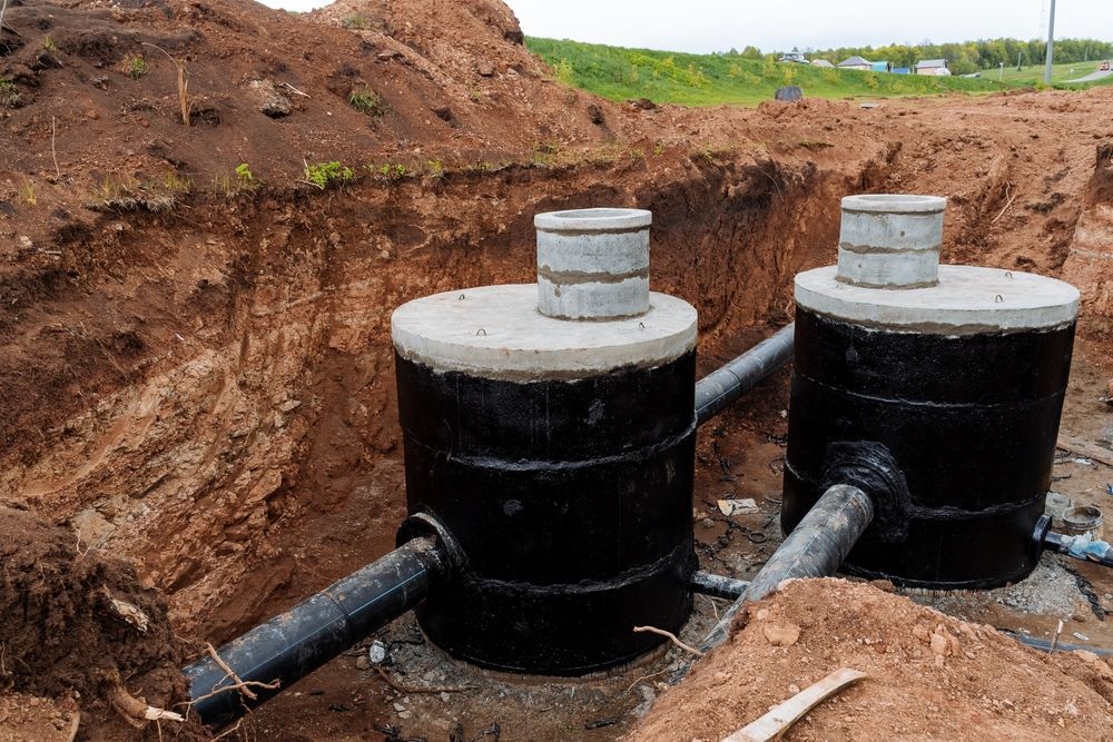 Two black septic tanks in an excavated area with concrete lids and connecting pipes.