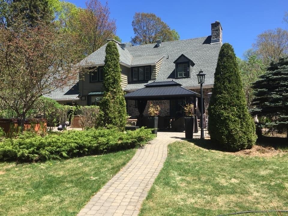 Par une journée ensoleillée, un chemin de pierre mène à une maison au toit gris et à un kiosque.