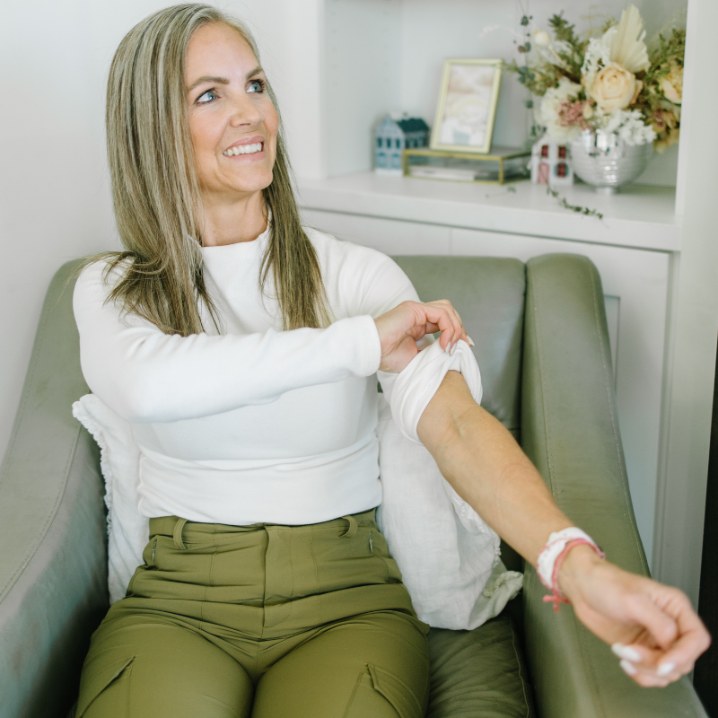 A woman is sitting in a chair with her arm outstretched and smiling.