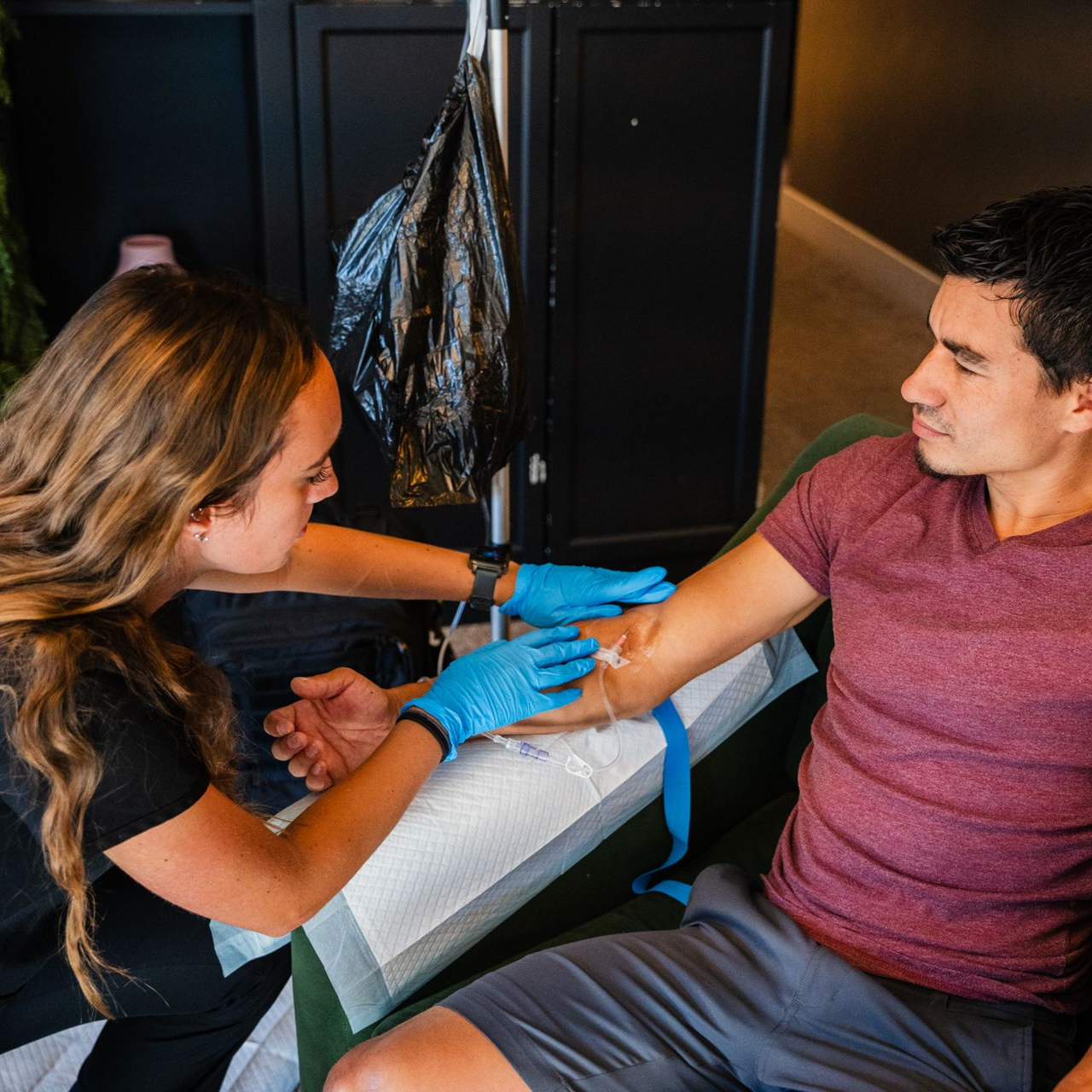 Woman in blue gloves administering a forearm treatment to a seated man indoors
