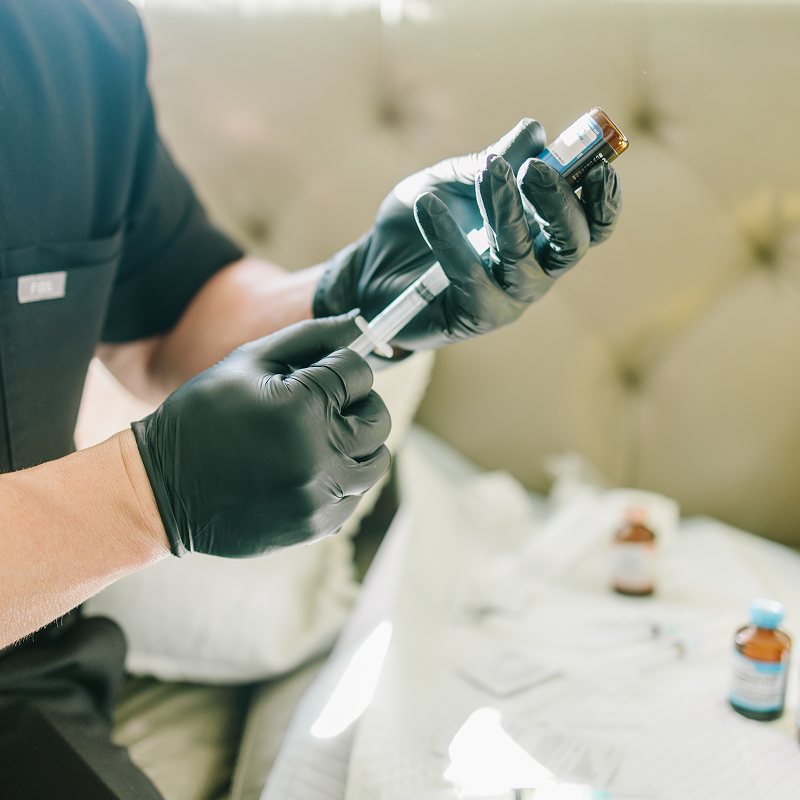 A person is holding a syringe next to a bag filled with bottles