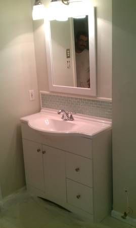 Bathroom vanity with a mirror and a person reflected in the mirror. White cabinet and light fixtures.