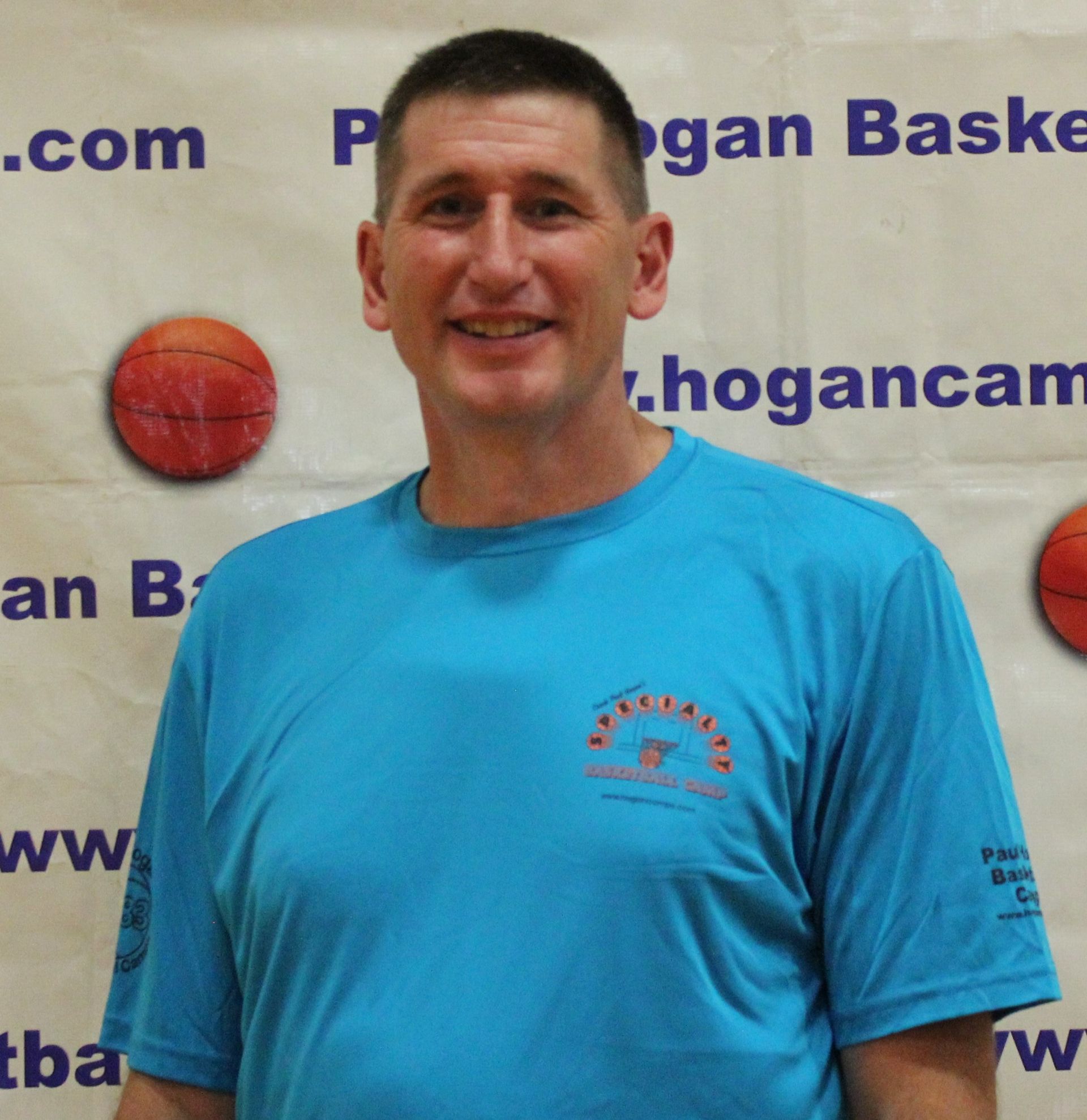 A man in a white shirt is standing in front of a basketball wall.