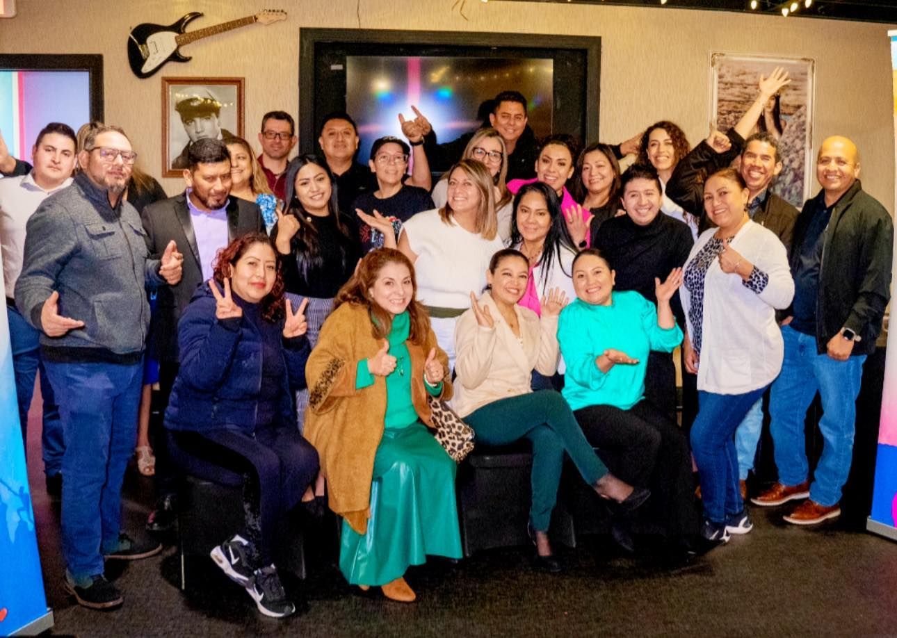 Group of women posing for a selfie; one smiling, others behind her. Bright event setting with backdrop.