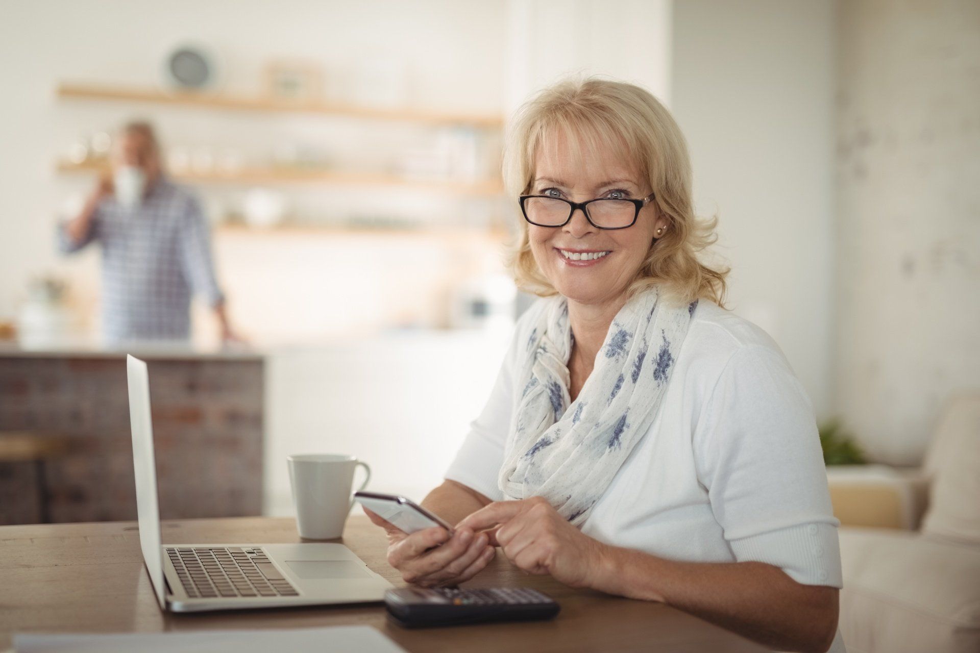 Older lady smiling, wearing glasses sitting at computer