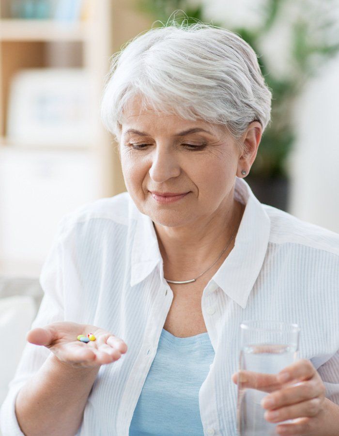 Woman with grey hair holding a glass of water in one hand and looking at pills in the other hand