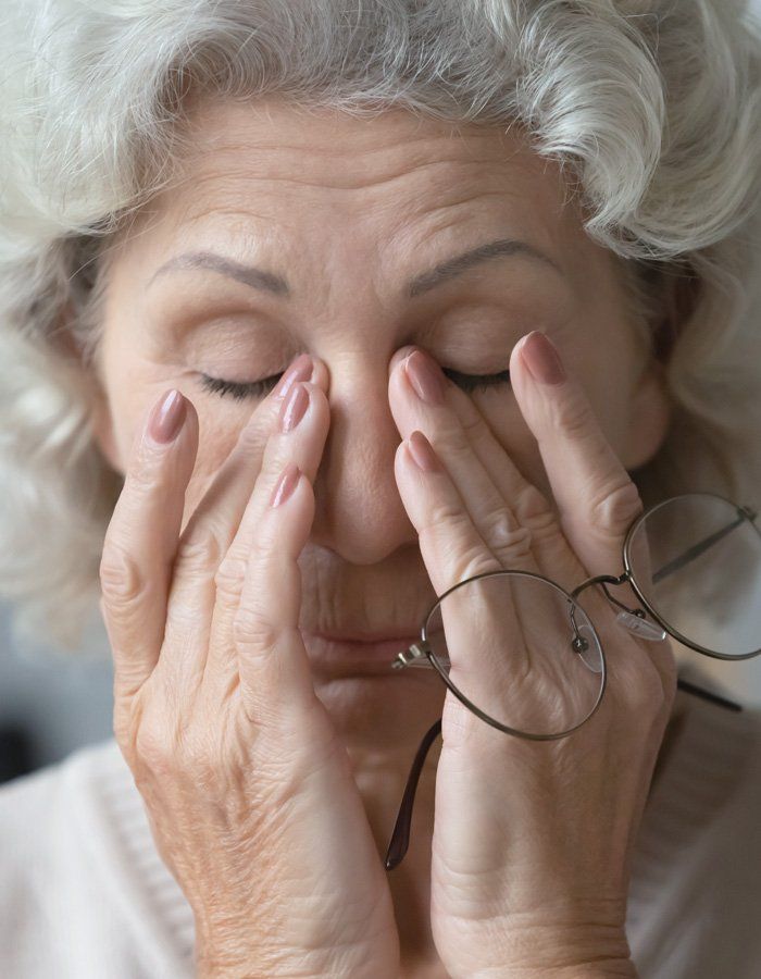 Older woman holding glasses and rubbing her eyes