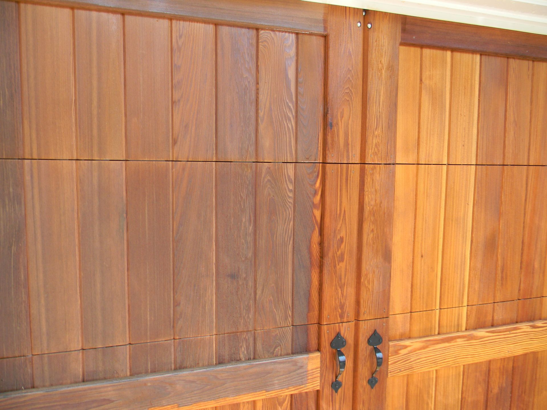 A close up of a wooden stained garage door with two handles.