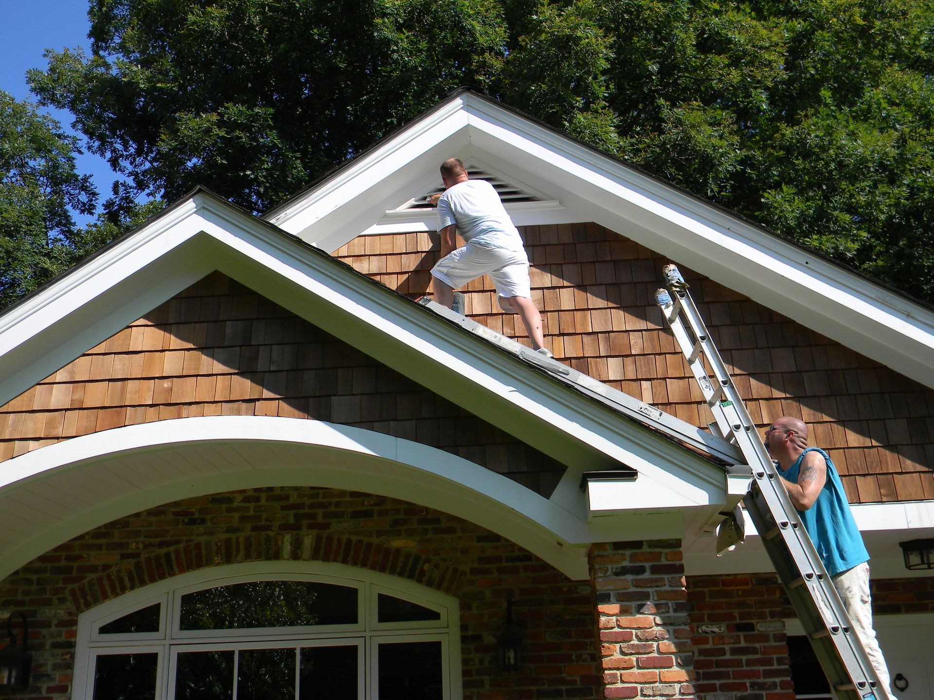 A man on a ladder repairs trim on a house