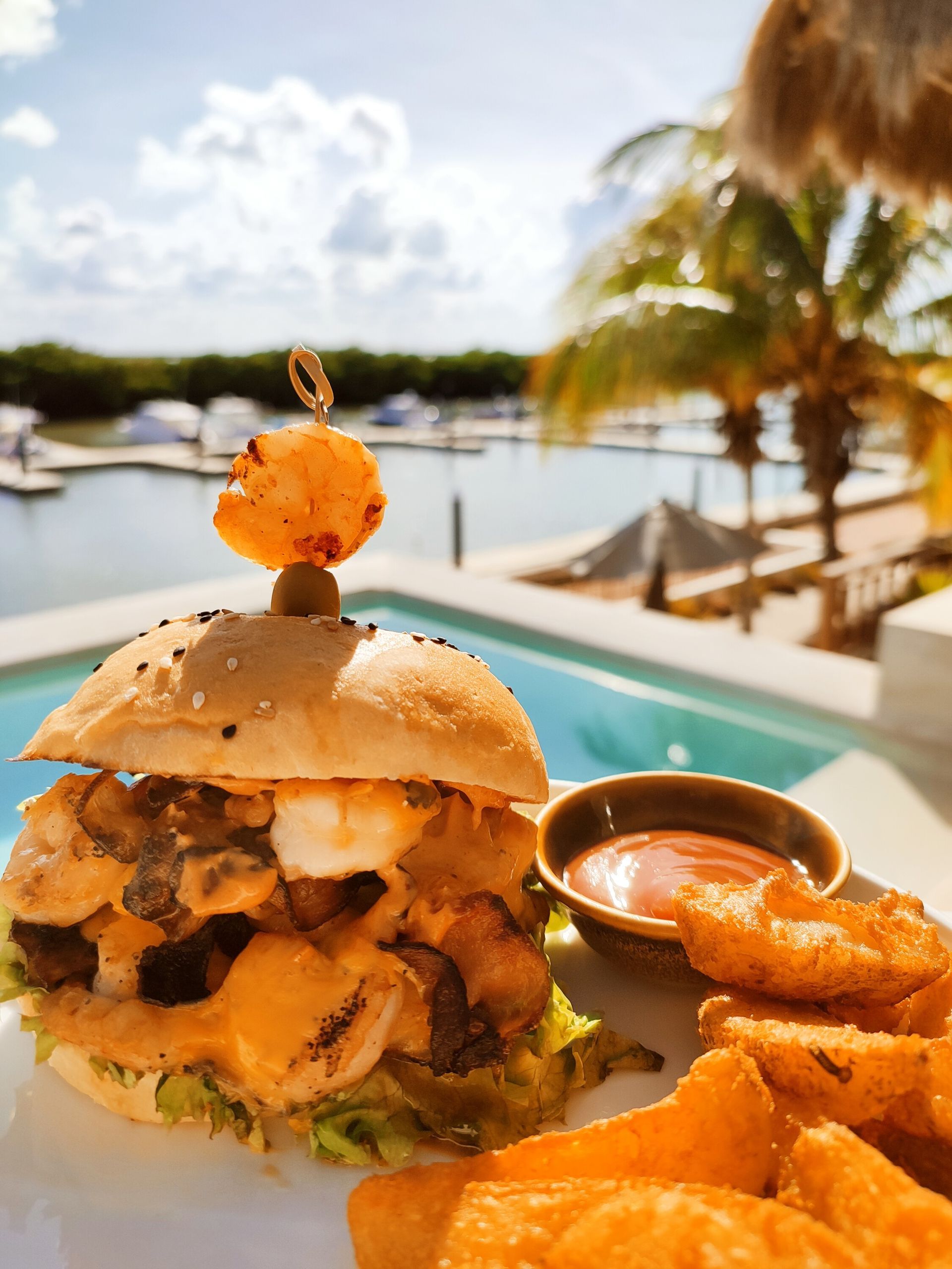 Una hamburguesa y patatas fritas están en una mesa al lado de una piscina.