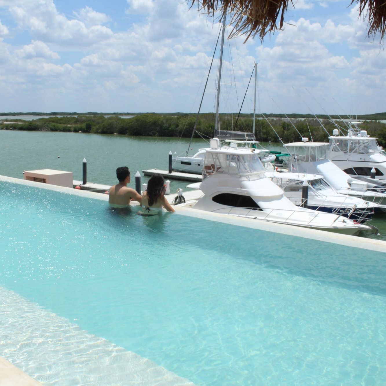 Una pareja se sienta en una piscina infinita con vistas a los barcos.