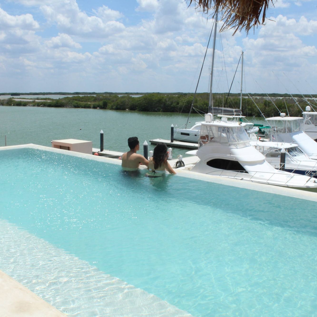Un hombre y una mujer se sientan en una piscina infinita con barcos en el fondo.