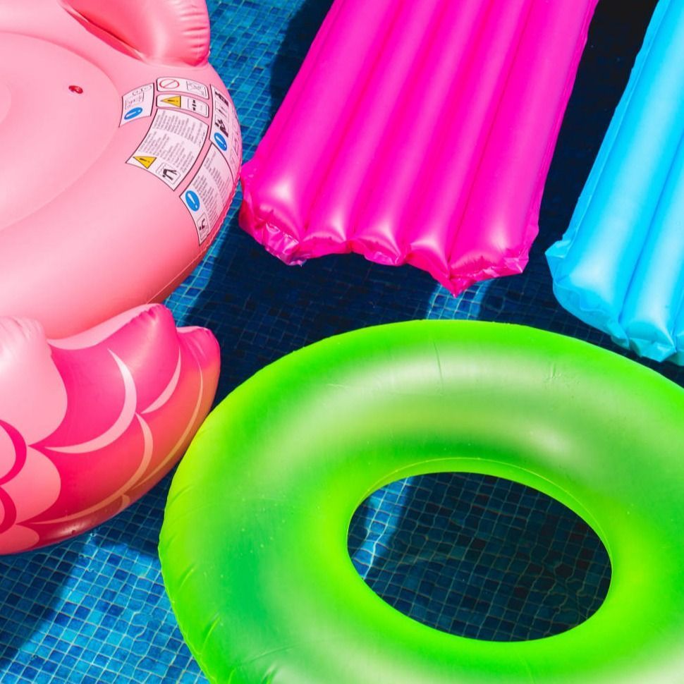 Un flamenco rosado flota junto a un anillo verde en una piscina.