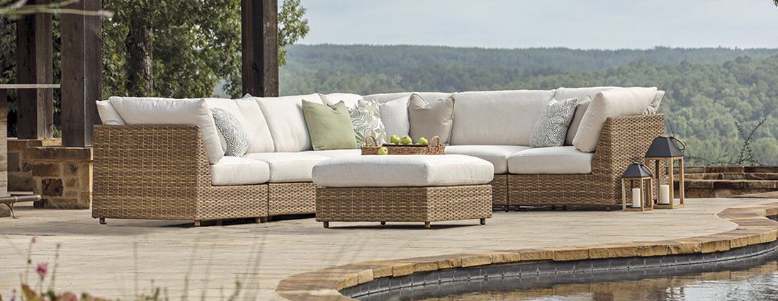 A wicker sectional couch is sitting on a patio next to a pool.