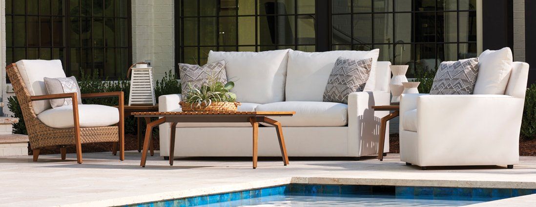 A patio with a couch , chairs , and a table next to a pool.