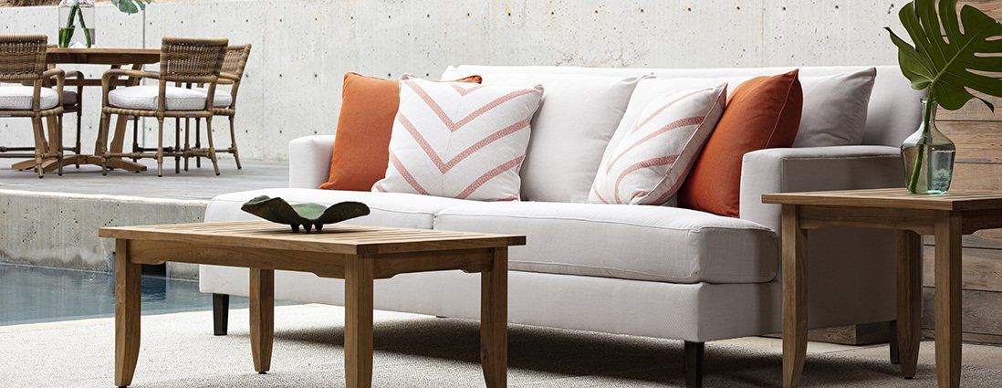 A white couch with orange pillows is sitting next to a wooden coffee table.