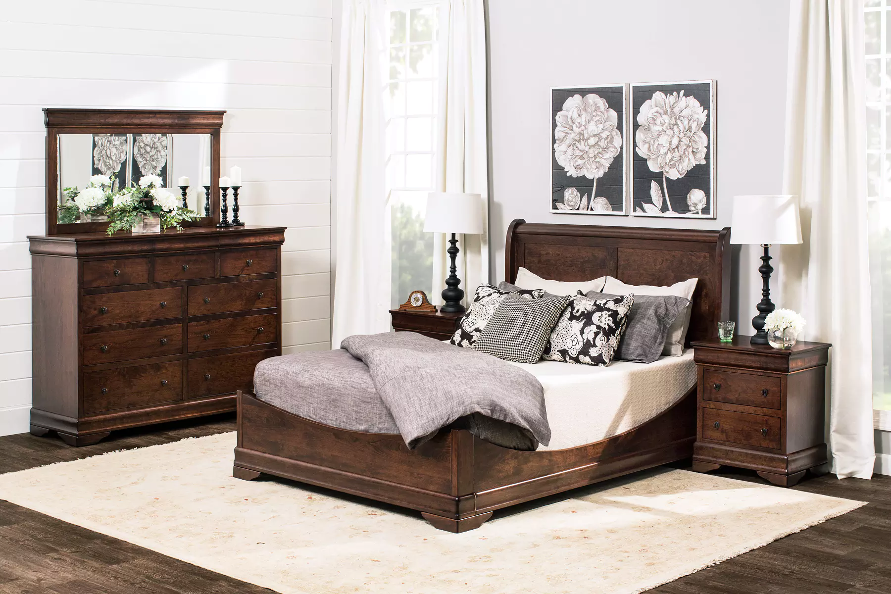 A bedroom with a bed , dresser , nightstand , mirror and rug.