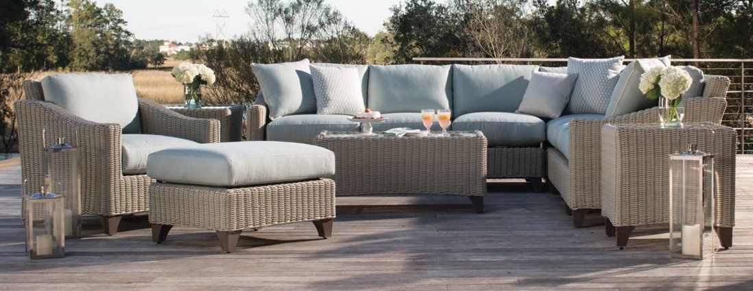 A wicker patio set with a couch , chairs , ottoman and coffee table.