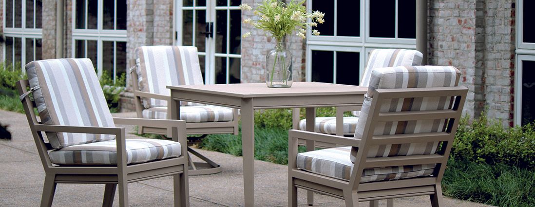 A table and chairs on a patio with a vase of flowers on it.