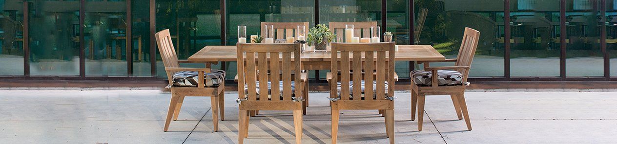 A wooden dining table and chairs on a patio in front of a building.