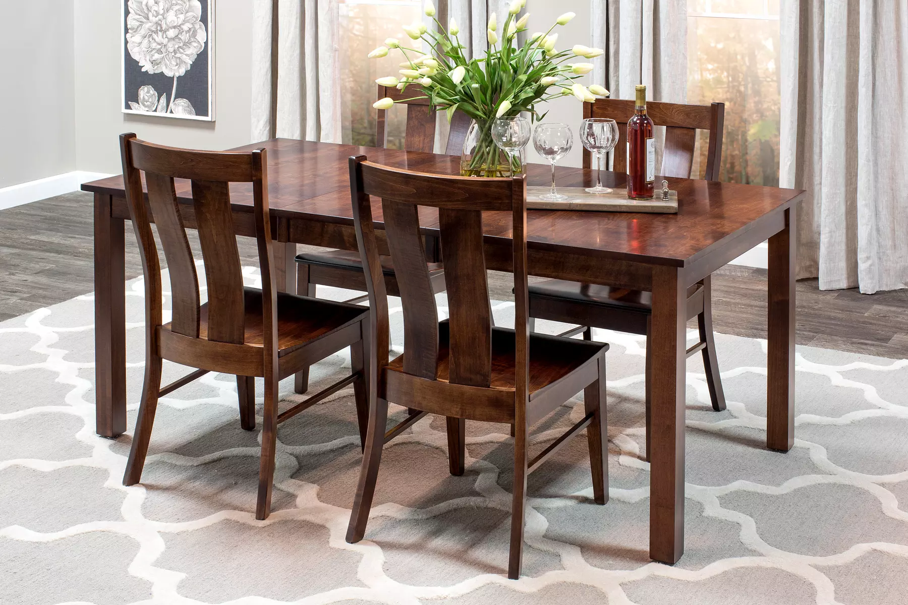 A dining room table and chairs with a vase of flowers on top of it.