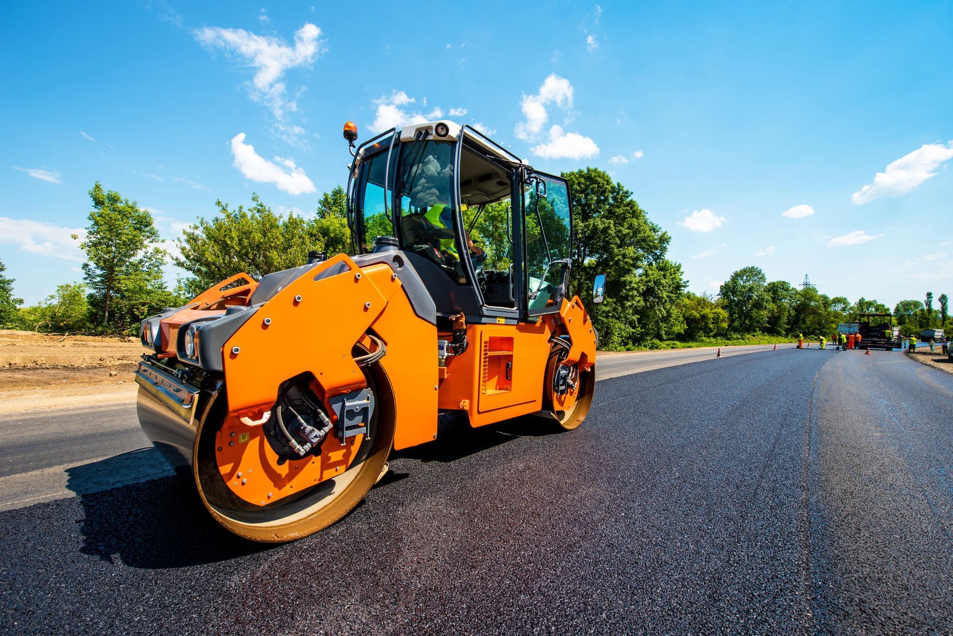 Una apisonadora naranja compacta asfalto fresco en una soleada obra vial.